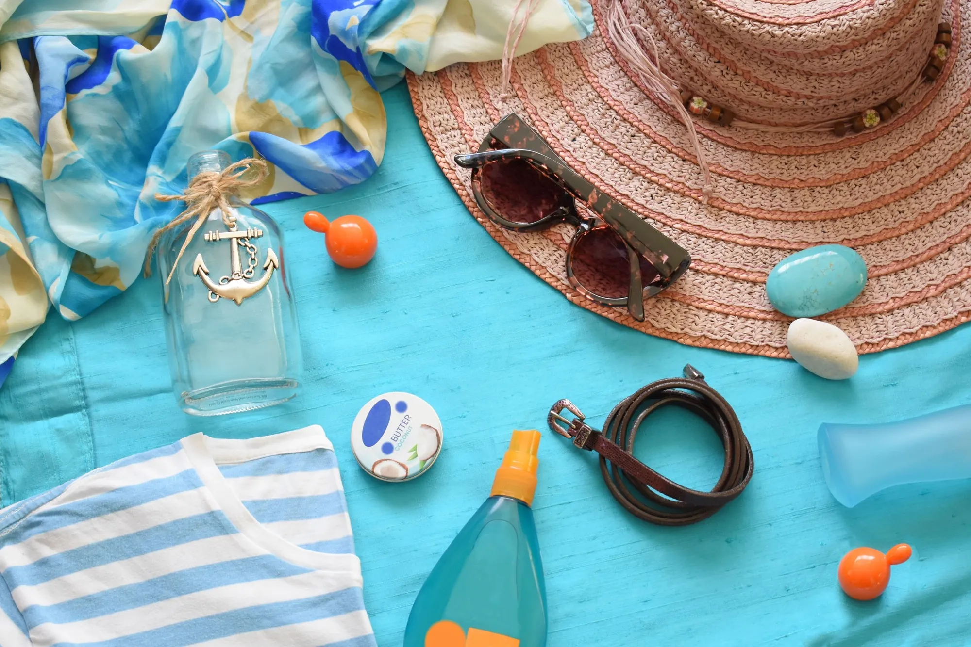 Hat, sunglasses, sunscreen, shirt, and other summer items laid out on a blue surface
